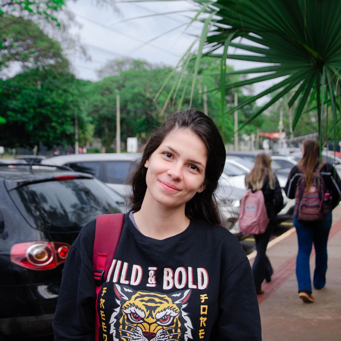 A young woman smiling on the street beside parked cars