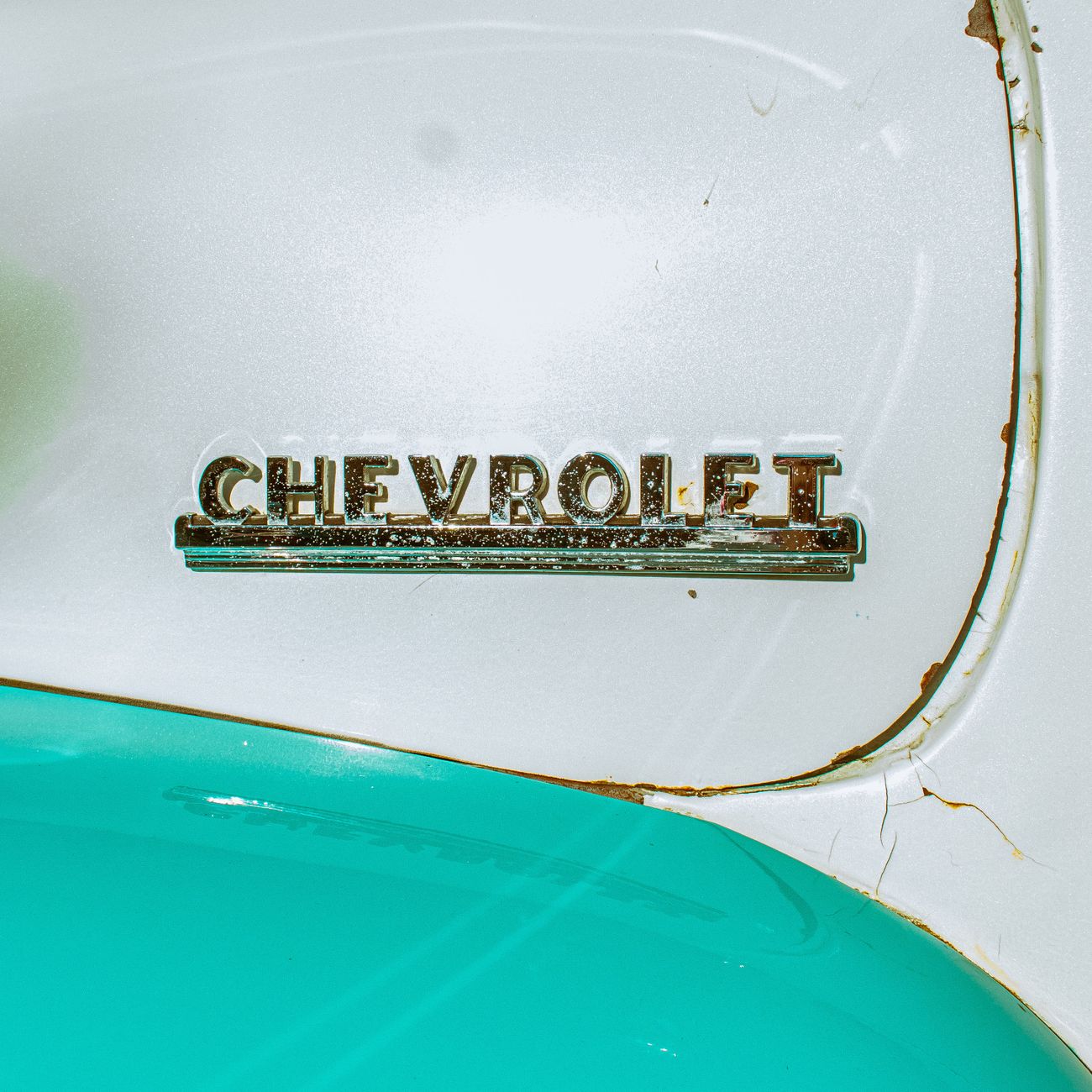A vintage Chevrolet emblem in turquoise paint with rust detail