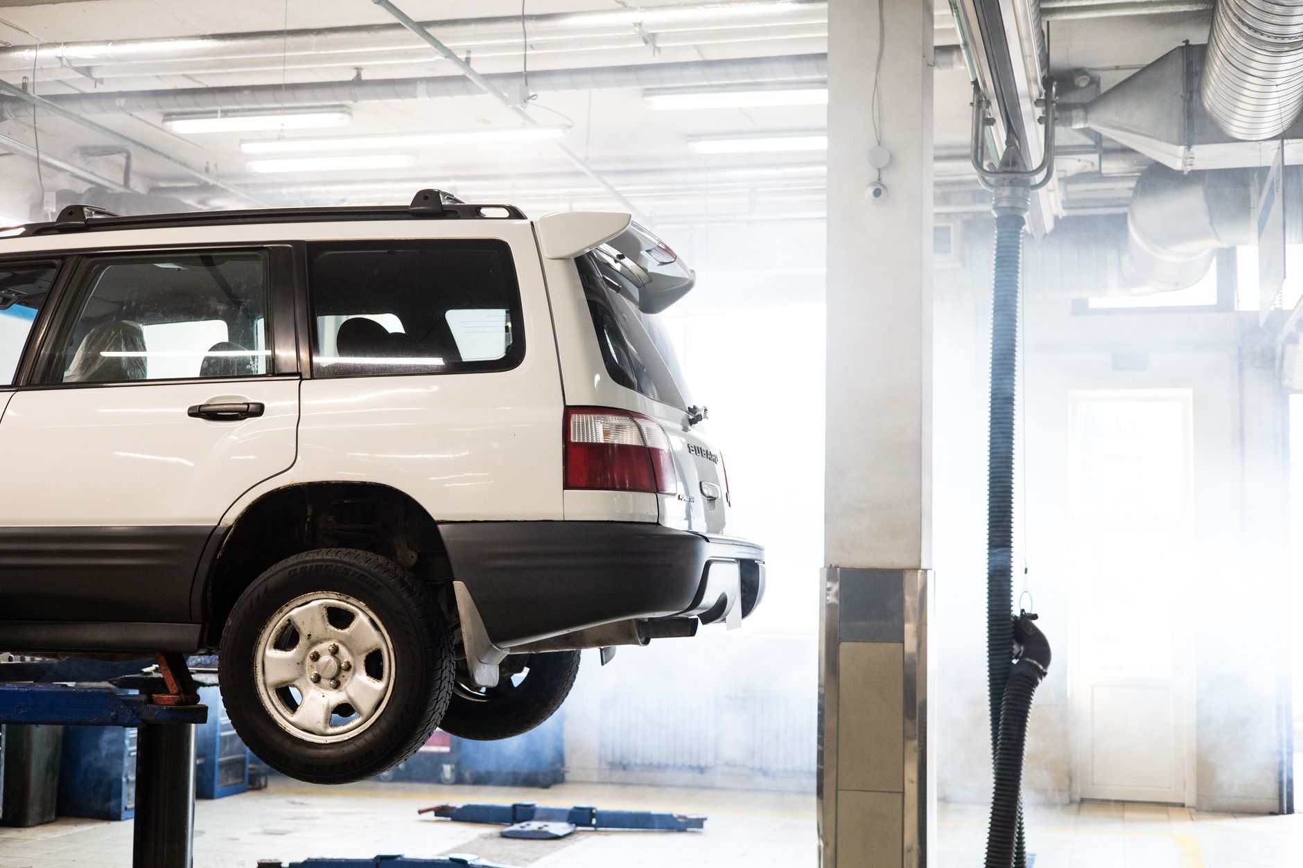 A white SUV raised on a lift inside the repair shop in daylight